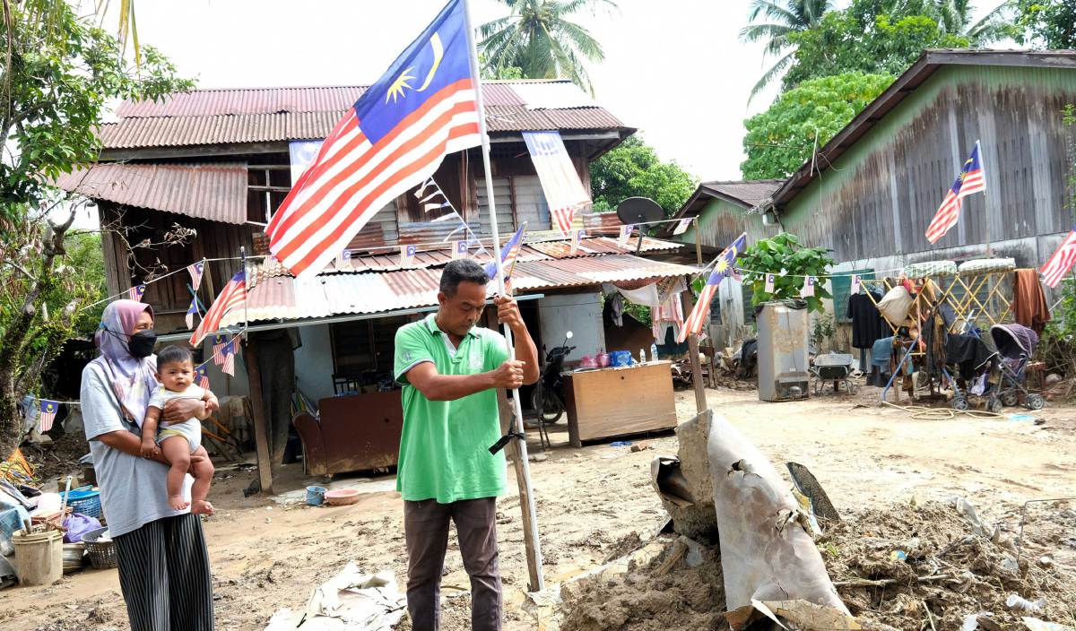 ROSLI mengibarkan Jalur Gemilang di perkarangan rumahnya yang masih diselaputi lumpur ketika ditemui dirumah mereka di Jalan Masjid Yan. FOTO BERNAMA