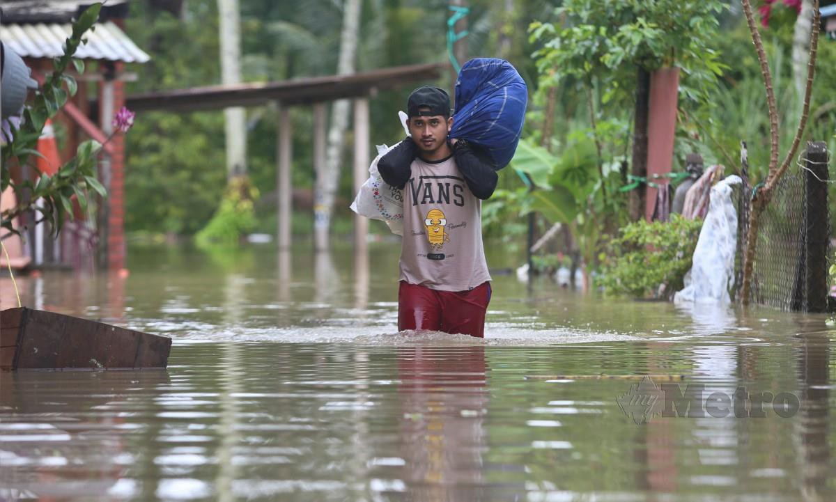 Penduduk Kampung Petaling, Tepoh, Kuala Nerus,  Muhammad Afham Ismail, 27 membawa barang peribadi  meredah banjir pada Selasa lalu. FOTO Ghazali Kori.