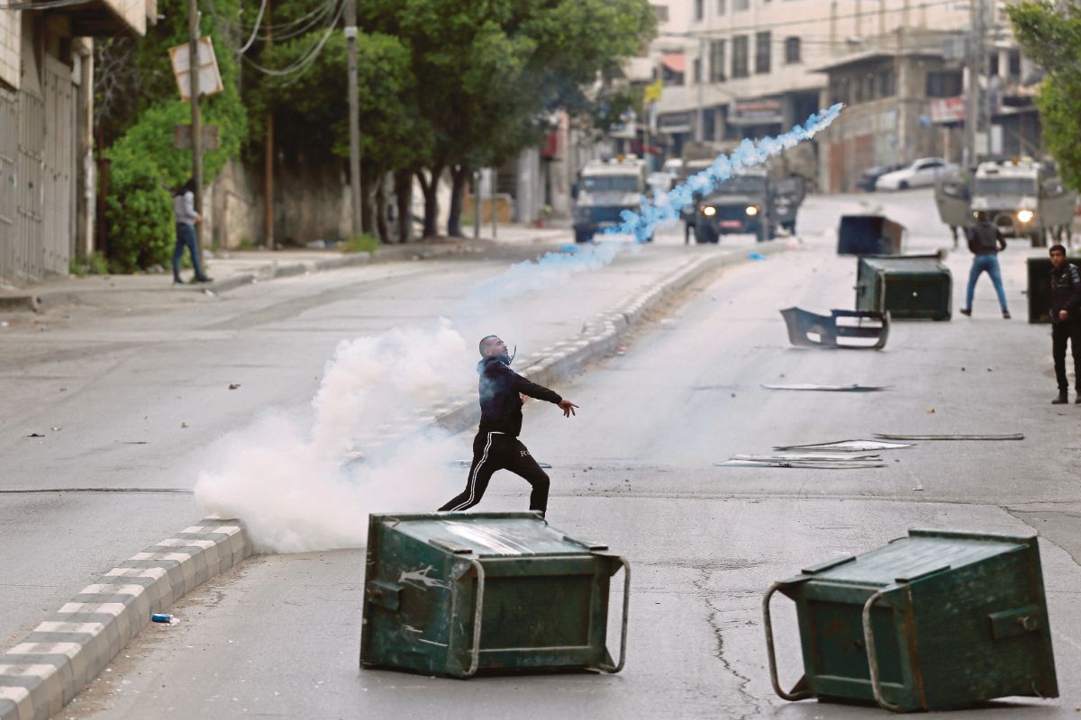 LELAKI Palestin mengutip dan membaling semula kanister gas pemedih mata yang dilepaskan tentera Israel ketika pertempuran di Nablus.  FOTO EPA 