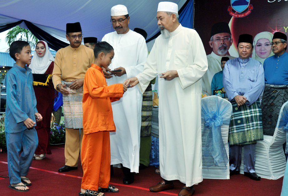 Tun Juhar menyerahkan sumbangan duit raya kepada anak yatim sambil diperhatikan Ramli (tiga dari kiri). FOTO Mohd Adam Arinin
