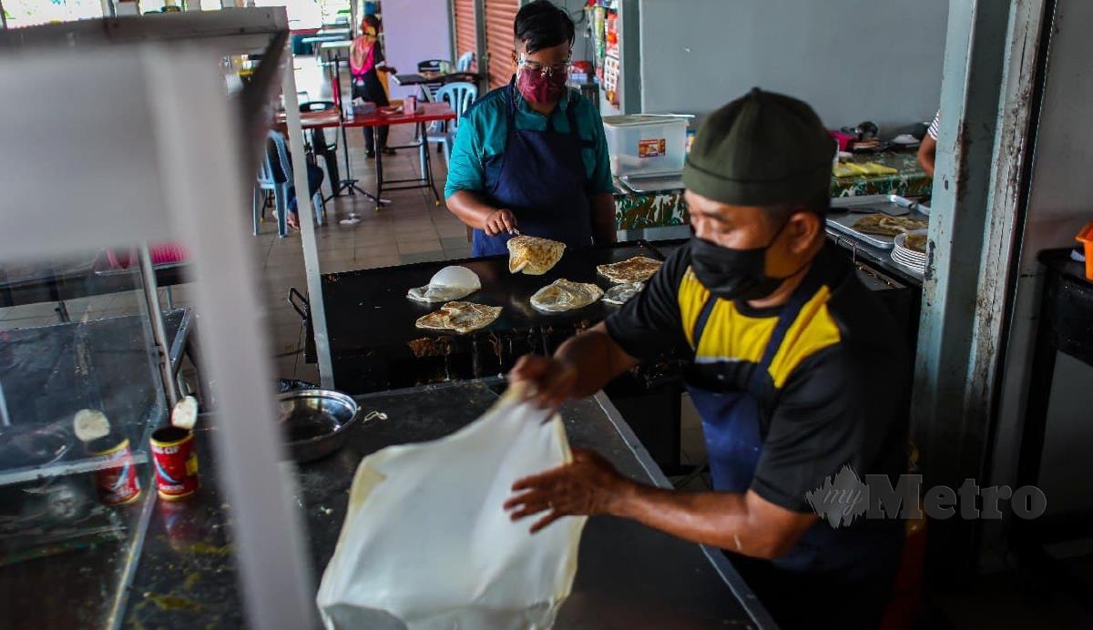 MUHAMMAD Ariff atau 'Buntat' (kiri) membantu bapanya Abdullah Kasim, menyediakan roti canai di Medan Selera Kubang Pasu. FOTO Luqman Hakim Zubir. 