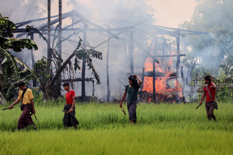 Gambar yang dirakam pada 7 September 2017 ini menunjukkan sekumpulan lelaki membawa pisau dan lastik berjalan berhampiran rumah yanng terbakar di perkampungan Gawdu Tharya dekat Maungdaw di negeri Rakhine, Myanmar. 