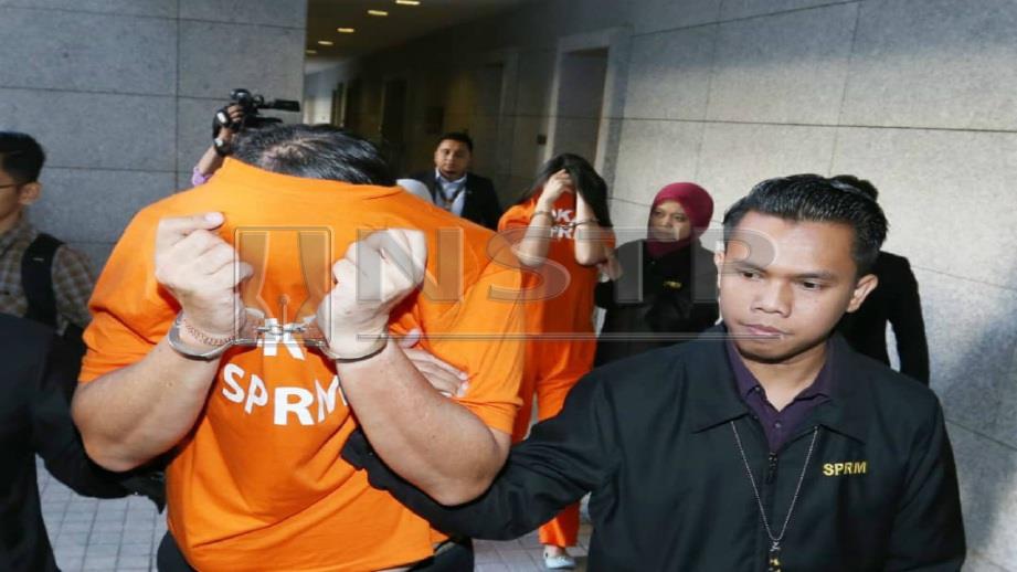 PEGAWAI SPRM mengiringi dua suspek (baju oren) untuk permohonan reman di Mahkamah Majistret Putrajaya, hari ini. Foto AHMAD IRHAM MOHD NOOR