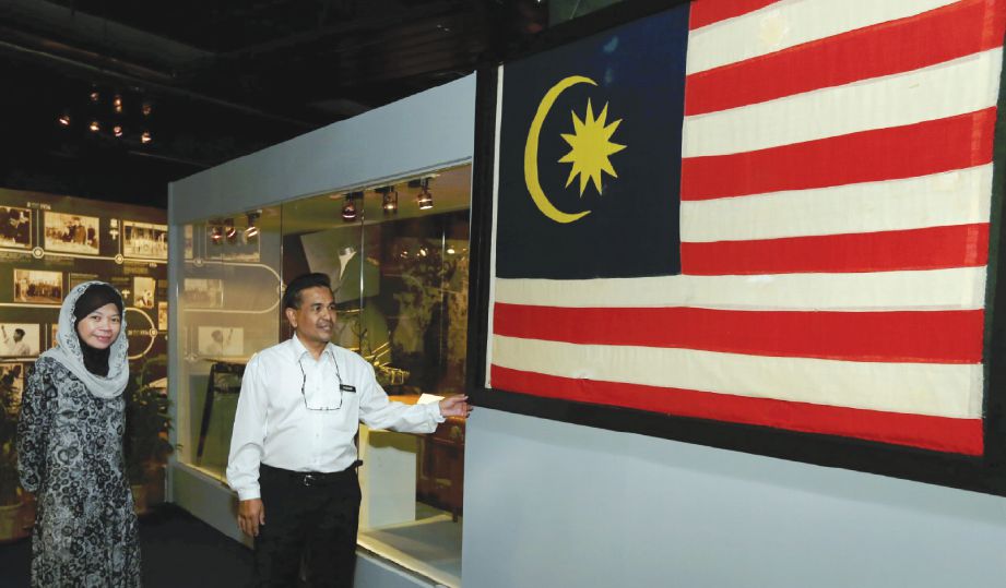 KURATOR Kanan Muzium Negara, Roselawati Abdullah (kiri) dan Penolong Kurator Muzium Negara, Badrul Hisham Abd Rahman menunjukkan bendera pertama Persekutuan Tanah Melayu.