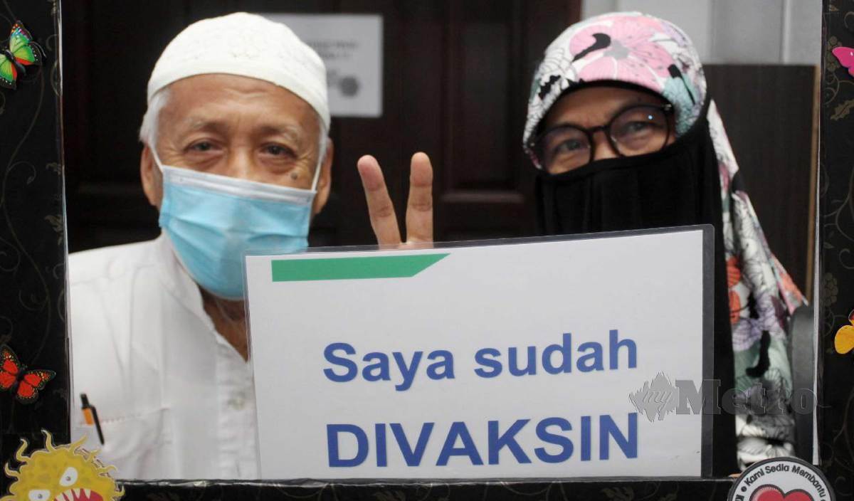 PASANGAN suami isteri, Siti Isah dan suami, Abdul Ghani memegang kad ‘Lindungi Diri, Lindungi Semua’ selepas menerima vaksin di Dewan Agensi Penguatkuasa Maritim Malaysia (Maritim Malaysia) Kelantan, Tok Bali. FOTO Nik Abdullah Nik Omar
