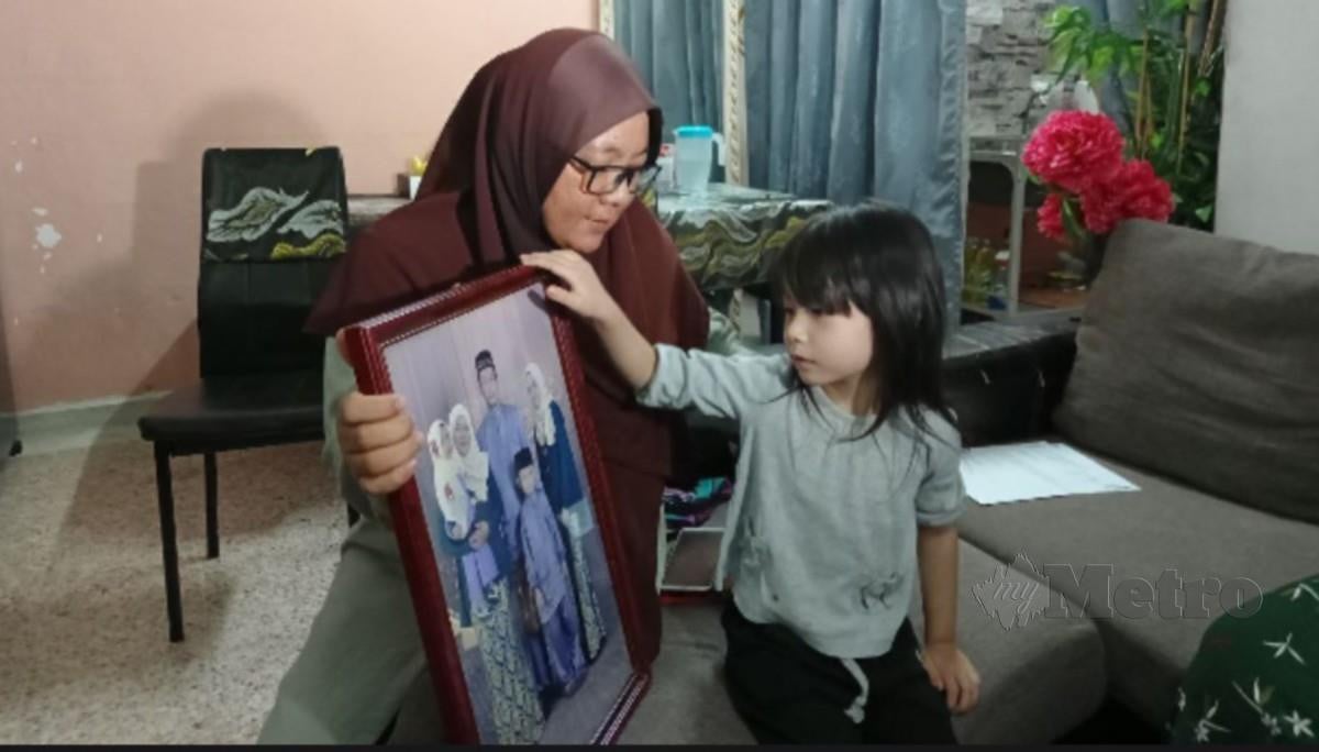 SOBOH Darmi bersama anak bongsunya, Aafiyah Raissa menunjukkan gambar keluarga. FOTO Meor Riduwan Meor Ahmad.