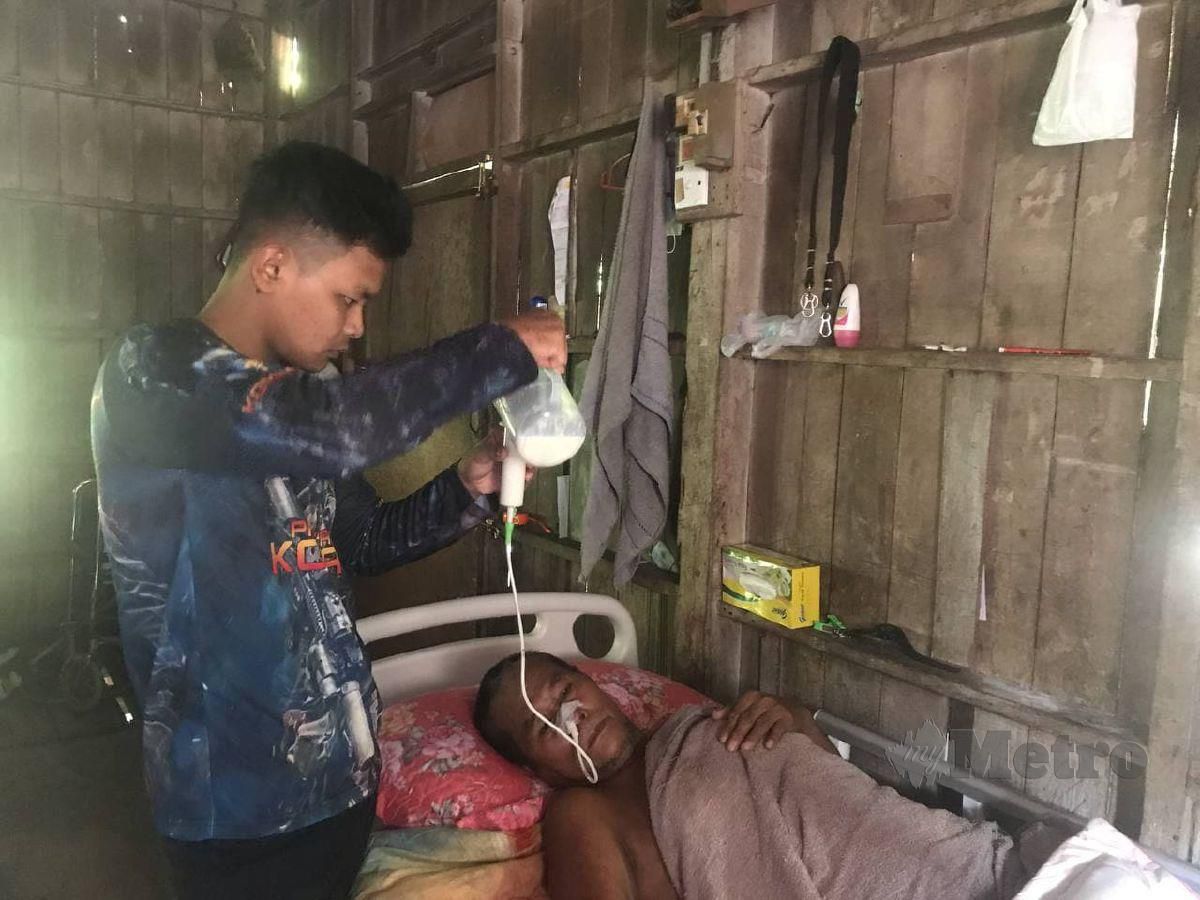 Mohamad Zuasraf memberi ayahnya minum susu melalui tiub yang dipasang di hidung ketika ditemui di rumahnya Kampung Padang Mokan, Peringat. FOTO HAZIRA AHMAD ZAIDI