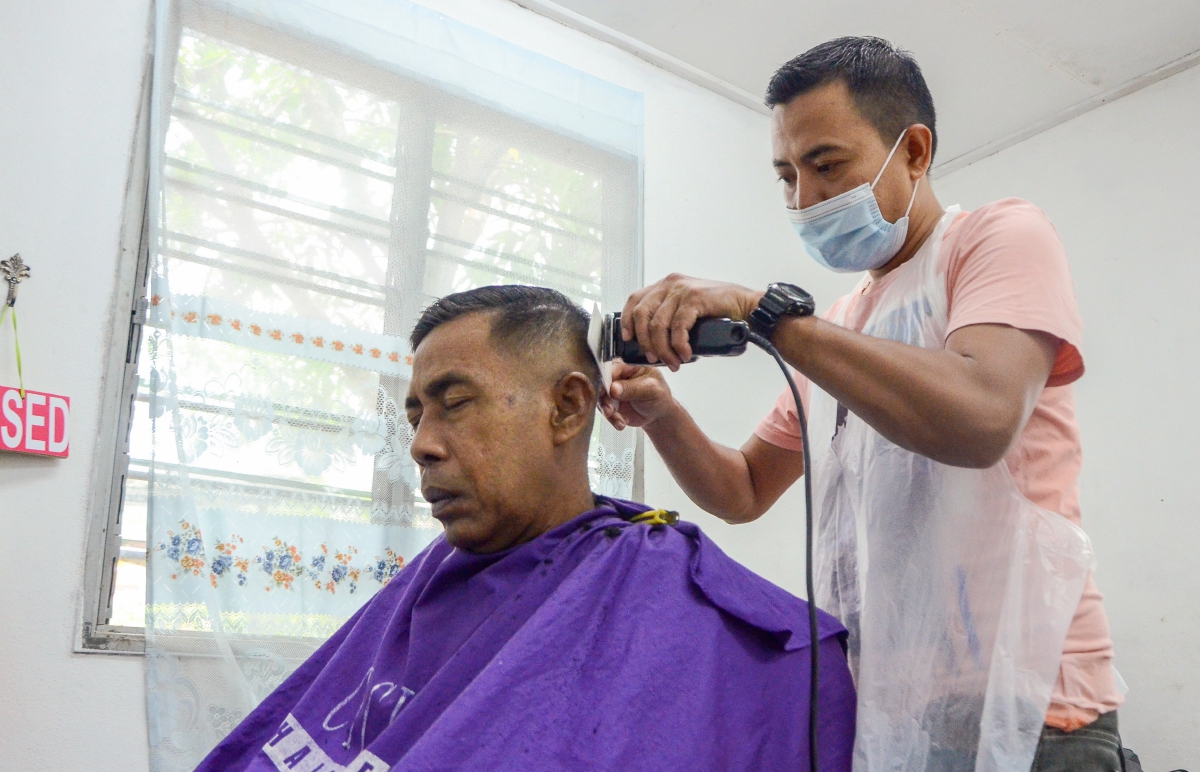 Harry Abdullah tekun memotong rambut pelanggannya ketika ditemui di kedainya di Kampung Padang Siam. FOTO BERNAMA