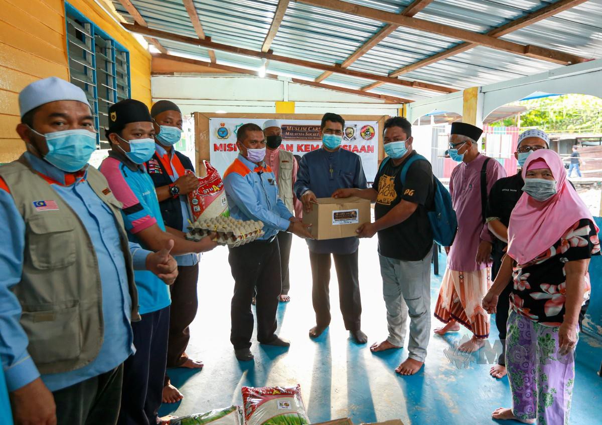 Dr Aliakbar (tengah) turut bersama Zulkifli (empat dari kiri) menyampaikan sumbangan kepada sebahagian penerima dari 150 penduduk Kampung Sungai Buaya di Tawau dalam Misi Santuni Asnaf Sabah anjuran Muslim Care Malaysia. FOTO ASWADI ALIAS.