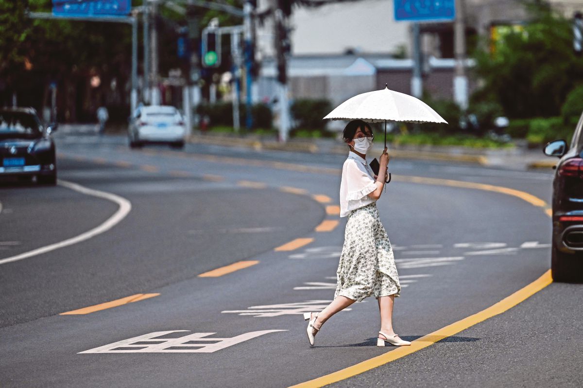 WANITA memakai pelitup muka ketika melintas jalan di Shanghai. FOTO AFP
