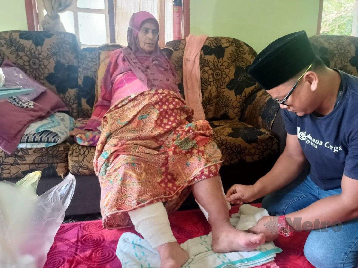 MOHD Firdaus membersihkan luka di betis ibunya ketika ditemui di rumah mereka di Kampung Che Deris di sini. FOTO Siti Rohana Idris