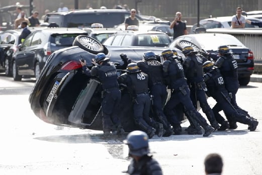 Anggota polis Perancis menterbalikkan kembali sebuah kereta yang diterbalikkan pemandu teksi yang merusuh di Paris. - Foto REUTERS