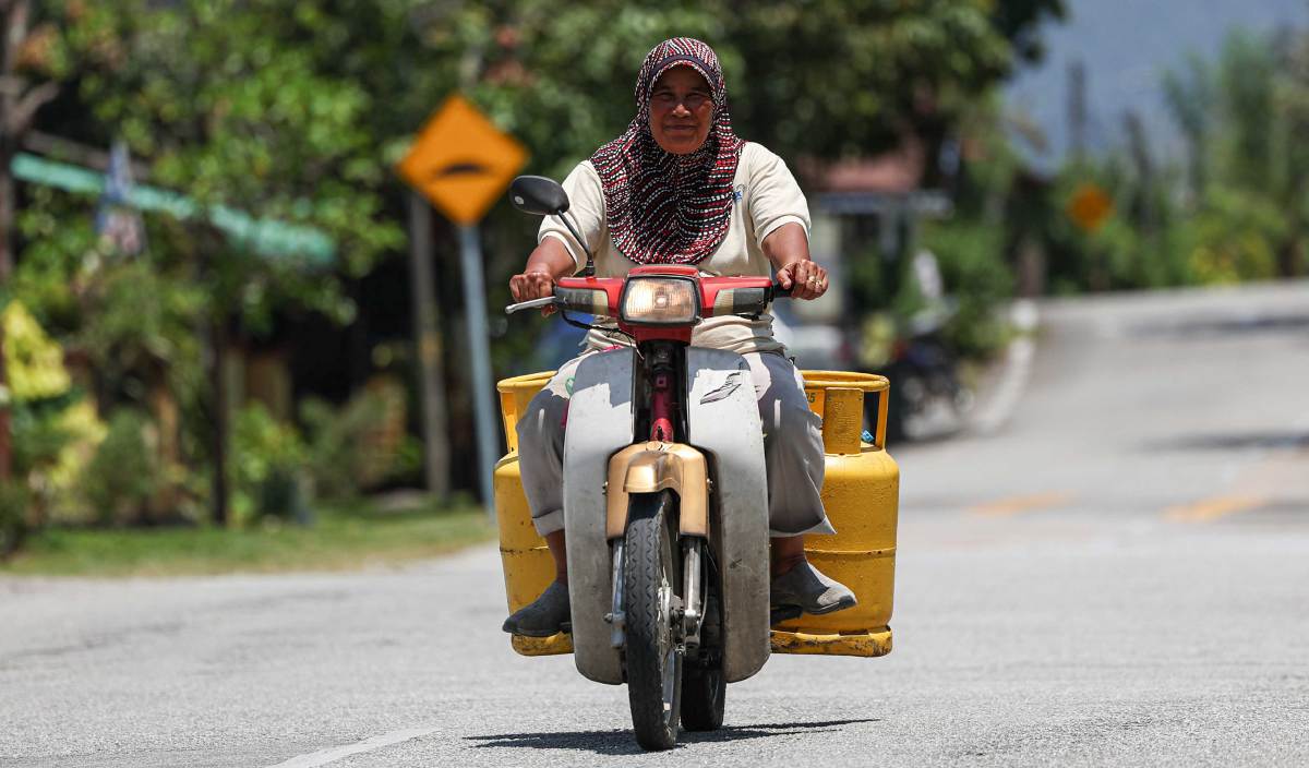 SAPARISAH menunggang motorsikalnya untuk menghantar tempahan tong gas di sekitar kawasan Kampung Datuk Ahmad Said Tambahan II. FOTO BERNAMA