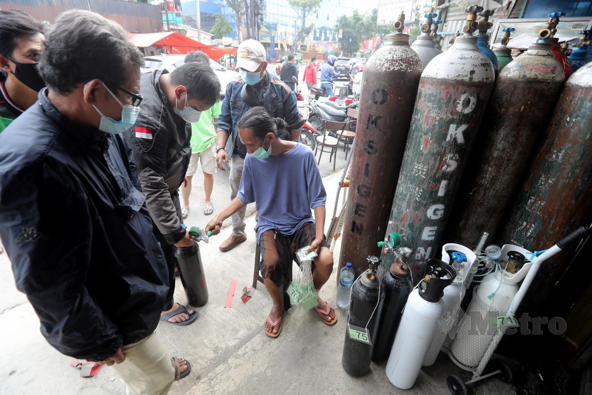 Seorang kakitangan memeriksa nombor giliran pelanggan yang mahu mendapatkan isian semula oksigen di Jakarta. - FOTO EPA