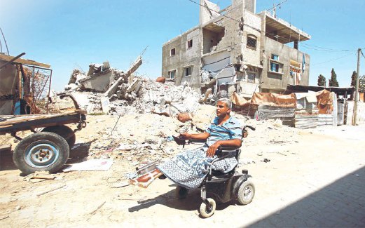 ALI Wahdan, guru matematik yang kini terpaksa menggunakan kerusi roda bermotor, melintasi runtuhan rumahnya di Beit Hanoun.