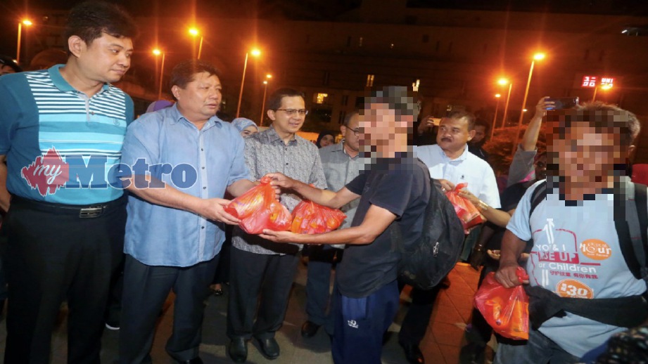 MAZLAN (dua kiri) menyampaikan sumbangan makanan kepada gelandangan sambil diperhatikan Amran (tengah) pada program Jalinan Kasih Jalanan di Johor Bahru, malam semalam. Foto HAIRUL ANUAR RAHIM