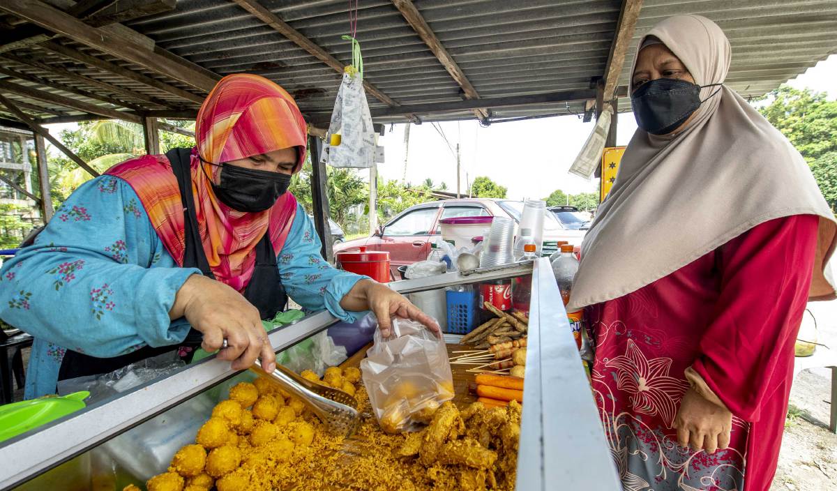 RAKIAH (kiri) melayan pelanggannya yang membeli ubi getuk di gerainya di Kampung Jambu Merah Melor. FOTO BERNAMA
