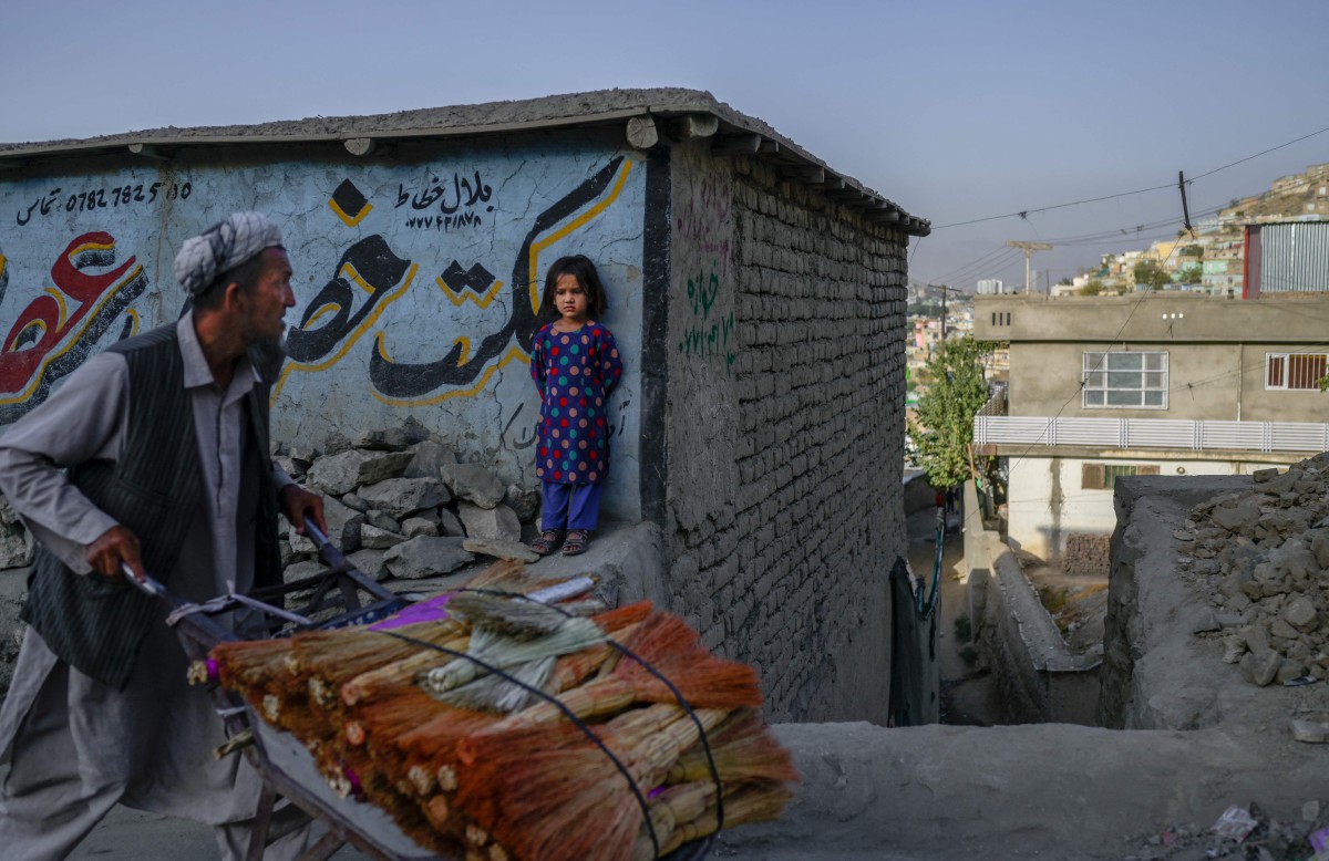 Peniaga menolak troli berisi penyapu sambil diperhatikan kanak-kanak perempuan di Kabul, Afghanistan. FOTO AFP.