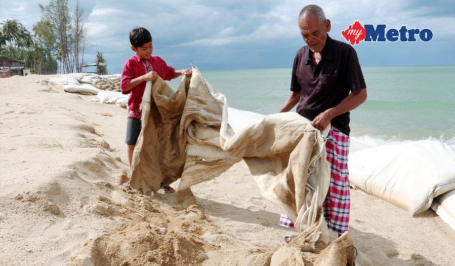 JUSOH dan cucunya menarik guni pasir yang tertimbus akibat hakisan. FOTO Faris Zainuldin