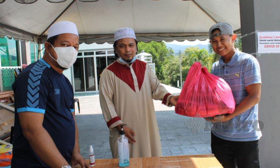 PENGERUSI Masjid Ibnu Khaldun, Mohd Husna Amin (tengah) menyerahkan pek mengandungi makanan asas kepada penerima bantuan. FOTO Mohd Amin Jalil.