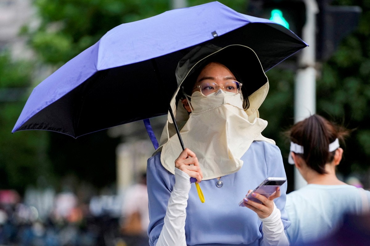 Seorang wanita mengenakan pelitup muka dan payung ketika berjalan di bawah cuaca panas di Shanghai, China. - FOTO Reuters