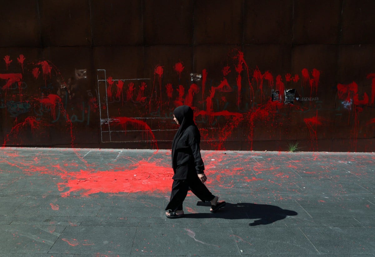 Seorang wanita berjalan di hadapan dinding yang dipenuhi cat merah di Beirut. - FOTO Reuters