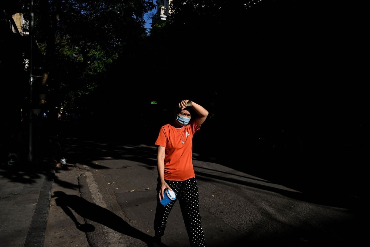 Seorang wanita berjalan dengan menutup wajahnya yang terkena cahaya matahari di Hanoi. - FOTO AFP