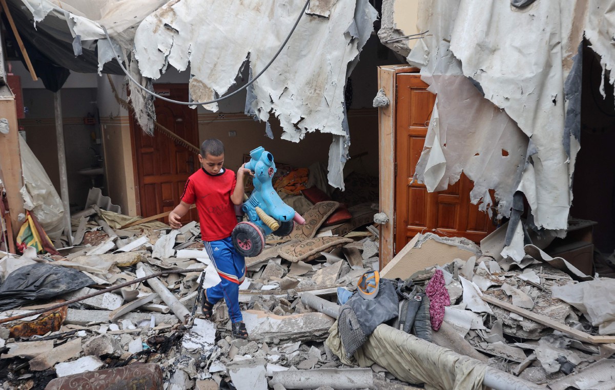 Seorang remaja Palestin menjumpai alat permainan di bawah runtuhan rumah di Rafah. - FOTO AFP