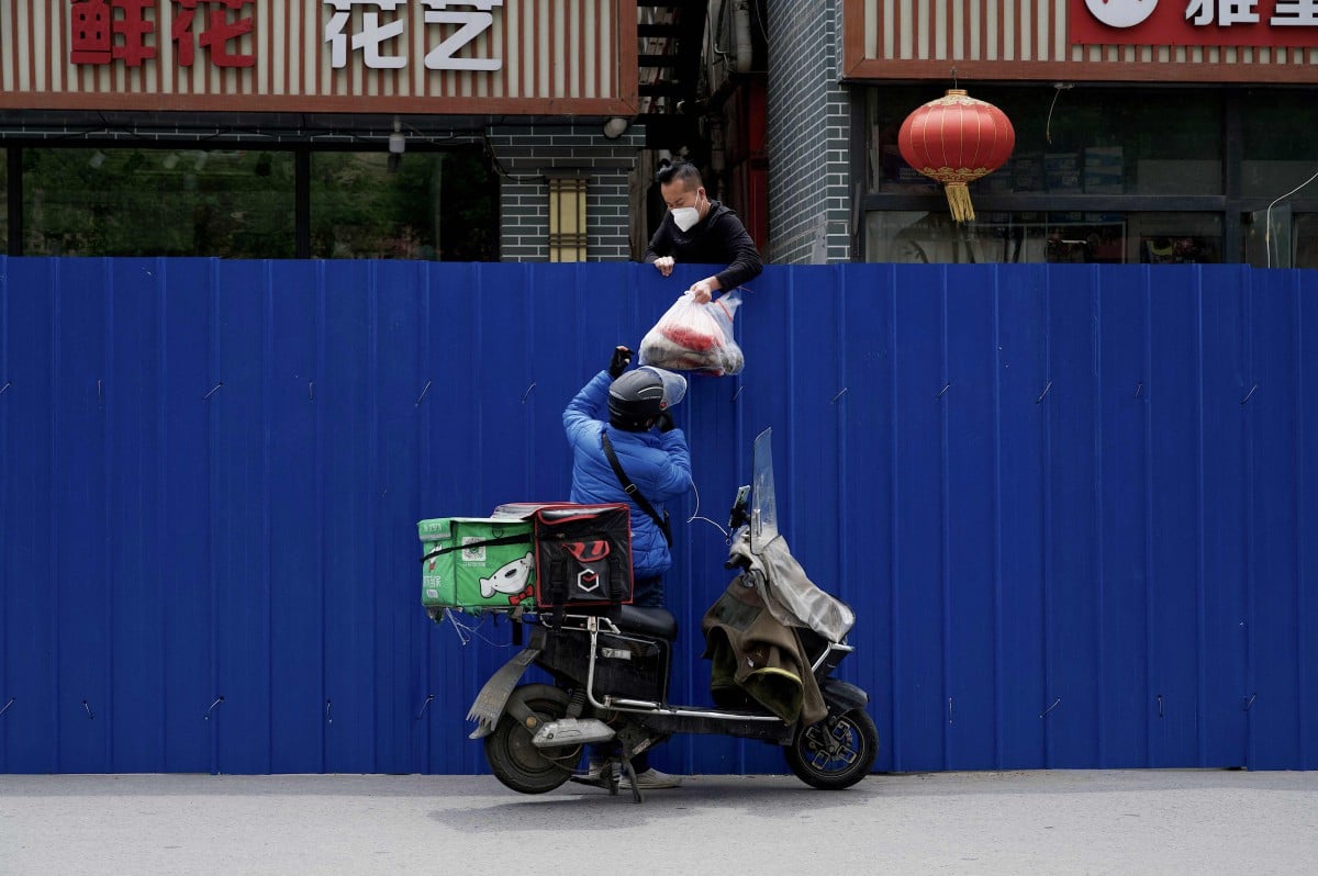 Seorang penghantar menyerahkan makanan kepada penduduk yang terkurung di Beijing. - FOTO AFP