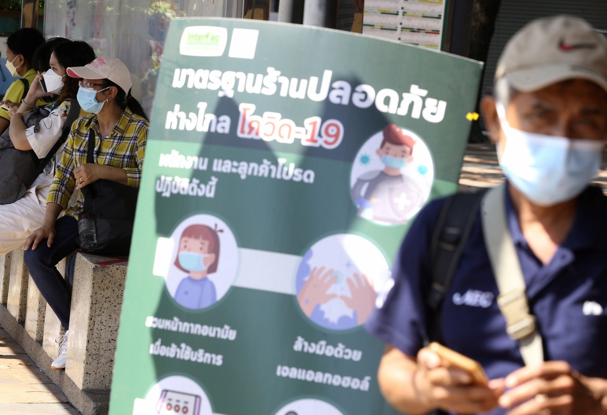 Orang awam memakai pelitup muka berjalan di hadapan poster peringatan berkaitann Covid-19 di Bangkok, Thailand. - FOTO EPA