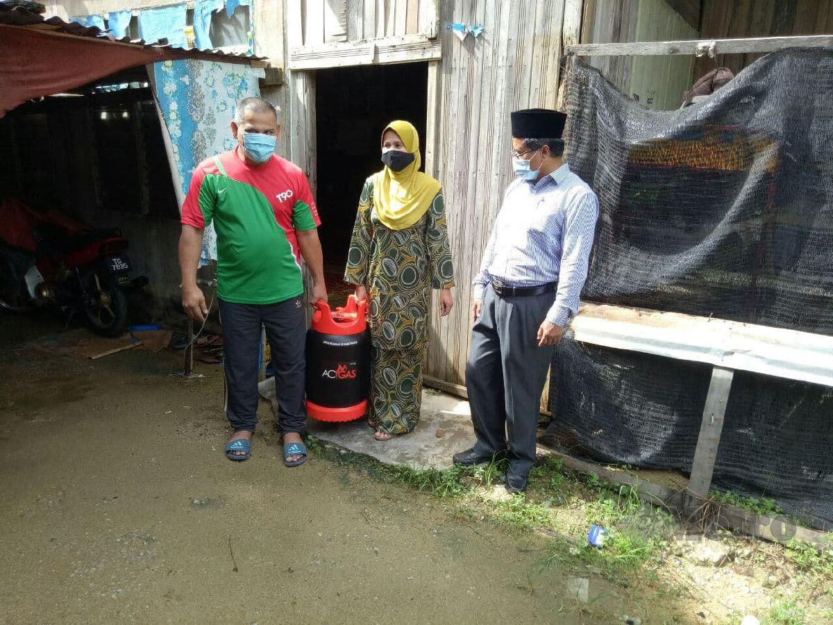 M Rozi Bidin (kanan) menyampaikan tong gas memasak kepada Ramlah pada program menyantuni golongan asnaf di Kampung Beladau Kolam, hari ini. FOTO Baharom Bakar