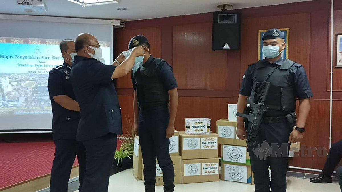 DATUK Shafien Mamat memakaikan pelindung muka kepada seorang anggota polis sebagai gimik sempena majlis penyerahan pelindung muka dan vitamin. FOTO Siti Rohana Idris