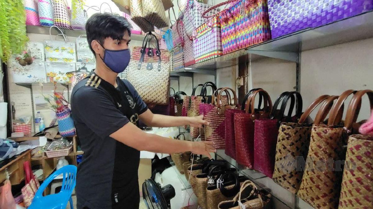 Muhammad Afiq sedang menyusun beg yang dijual di kedainya ketika ditemui di pekan Rantau Panjang, hari ini. FOTO Syaherah Mustafa