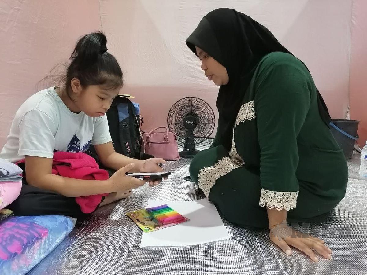 AMUNA menemani anak sulungnya ketika melaksanakan pembelajaran di rumah (PdPR) ketika berada di PPS Dewan Datuk Seri Panglima Dun Banir. FOTO Yun Mikail