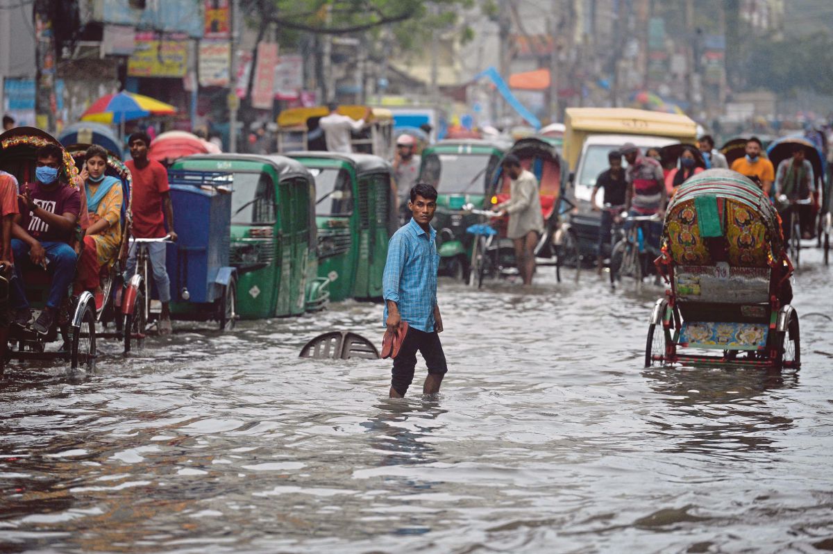 PENUMPANG melalui jalan yang dipenuhi air setelah hujan lebat di Dhaka. FOTO AFP