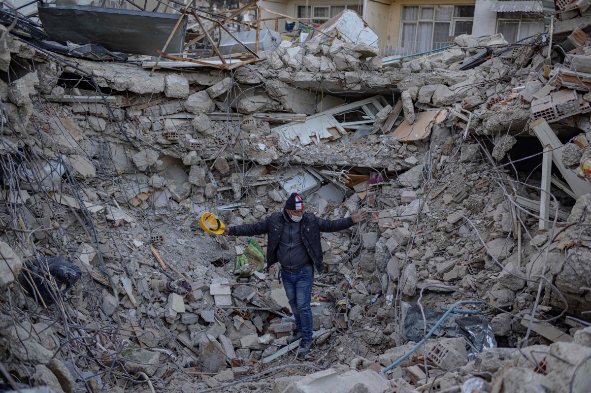 Seorang lelaki berdiri di atas longgokan serpihan bangunan yang runtuh di Antakya, Turkiye. - FOTO AFP