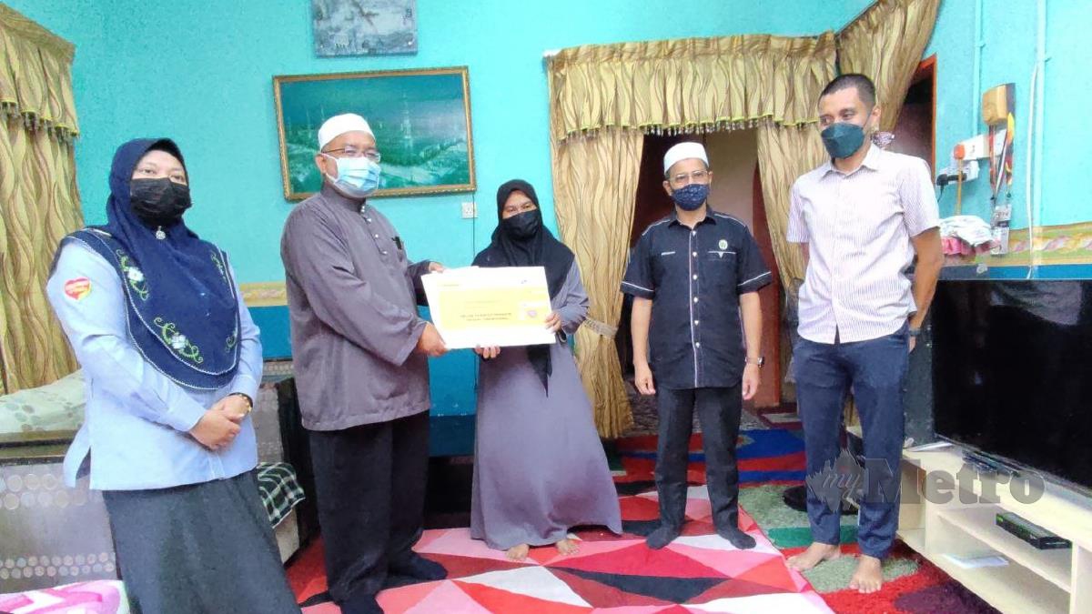 WAN Sukairi (dua dari kiri) menyerahkan faedah pengurusan jenazah sebanyak RM2,000 dan pencen penakat kepada Siti Mastura. FOTO Nurul Fatihah Sulaini