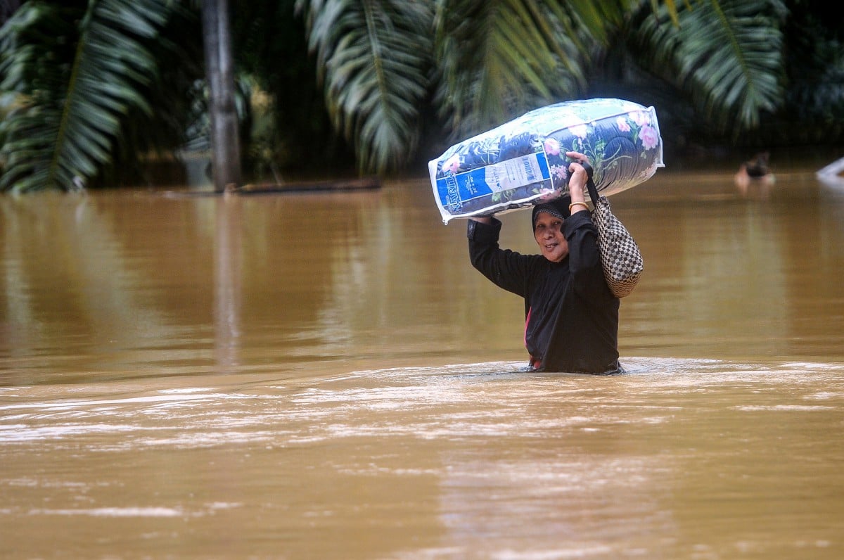 Seorang penduduk Robiah Salim, 65, meredah banjir untuk ke Pusat Pemindahan Sementara (PPS) dengan membawa barang keperluan selepas pulang melihat keadaan rumahnya ketika tinjauan di Kampung Pengkalan Ajal semalam. FOTO BERNAMA.
