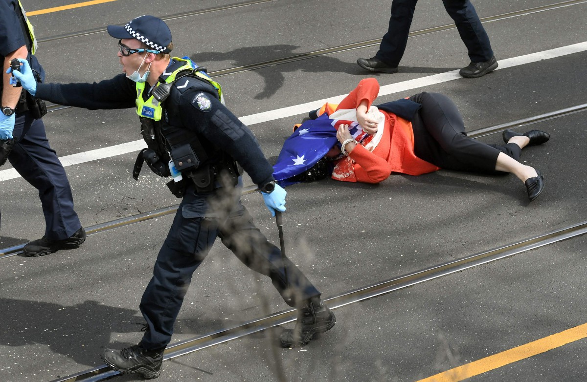 Seorang peserta protes jatuh akibat ditolak ketika pertembungan dengan anggota polis di Melbourne. - FOTO AFP