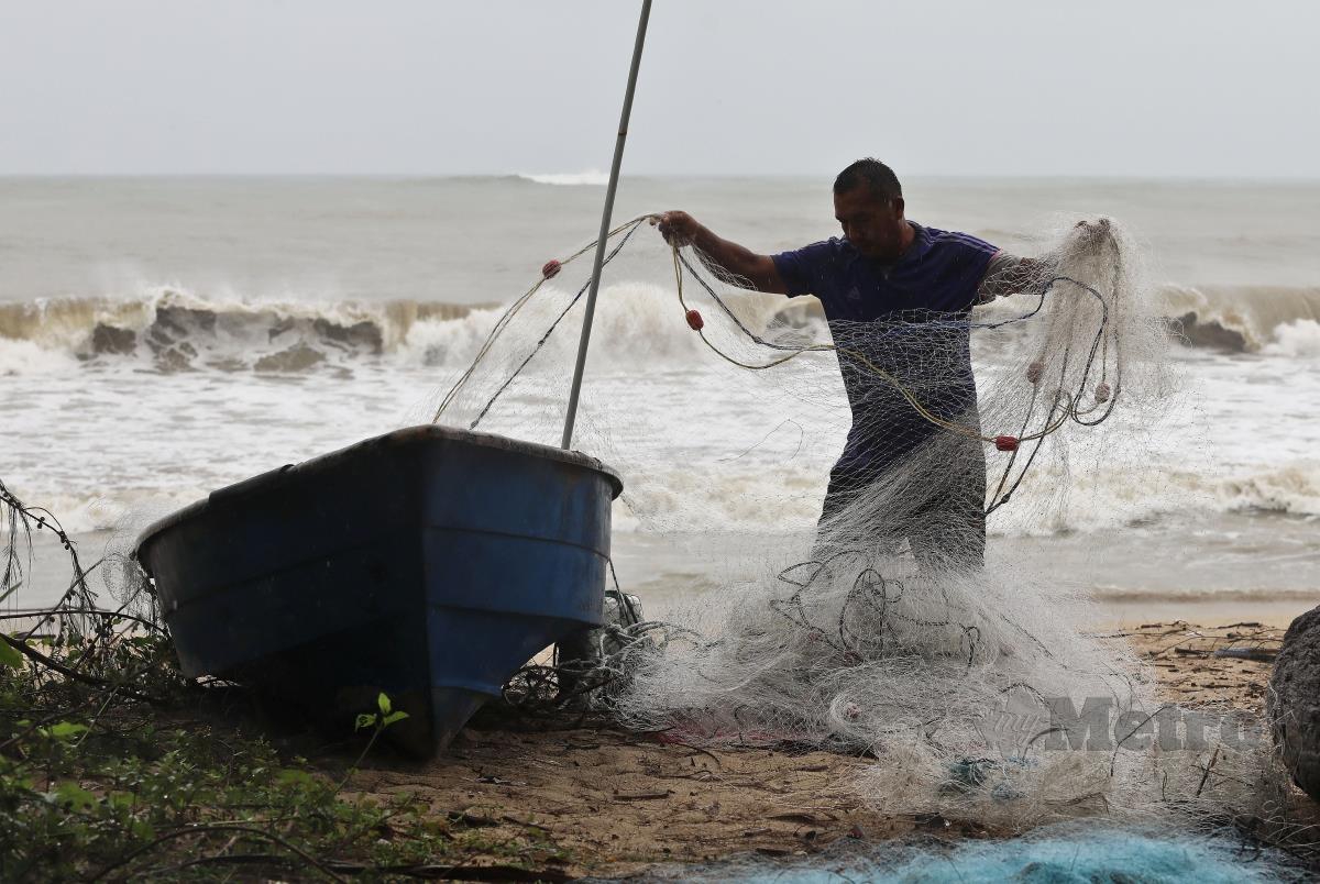 NELAYAN mengalihkan pukat dan bot ke tempat yang lebih tinggi sebagai persediaan susulan ombak besar dan air pasang di Pantai Rhu Renggeh. FOTO GHAZALI KORI