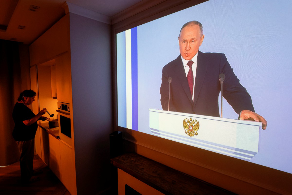 Seorang wanita mendengar ucapan Presiden Rusia, Vladimir Putin sambil memasak di rumahnya. - FOTO EPA