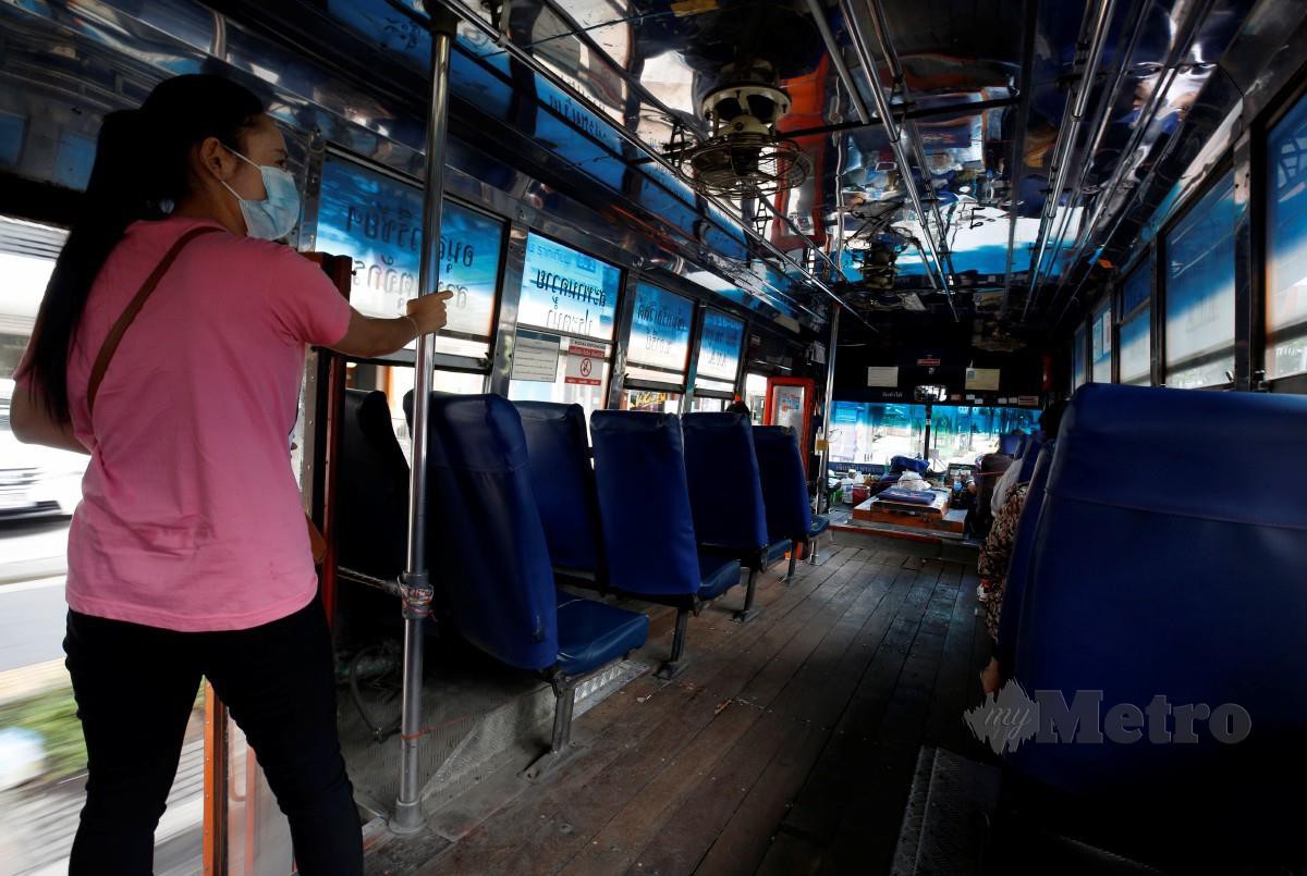 Seorang wanita mengenakan pelitup muka berdiri di dalam bas di Bangkok, Thailand. Negara berkenaan mengenakan sekatan lebih ketat di 13 wilayah termasuk Bangkok selepas berlaku lonjakan kes Covid-19. - FOTO EPA