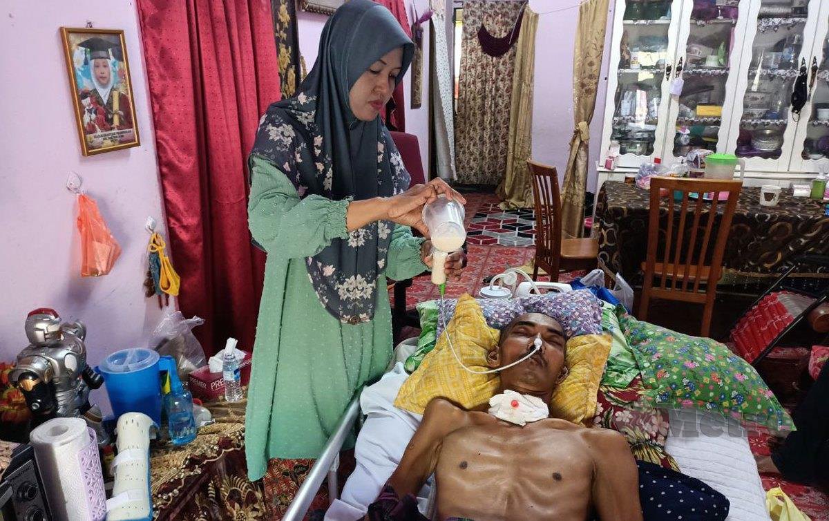 ASLEERAINI memberi susu khas kepada suaminya Mohd Nawi Mustapha, 44, yang terlantar akibat strok otak di rumahnya di Kampung Berlian, di sini. FOTO Siti Rohana Idris