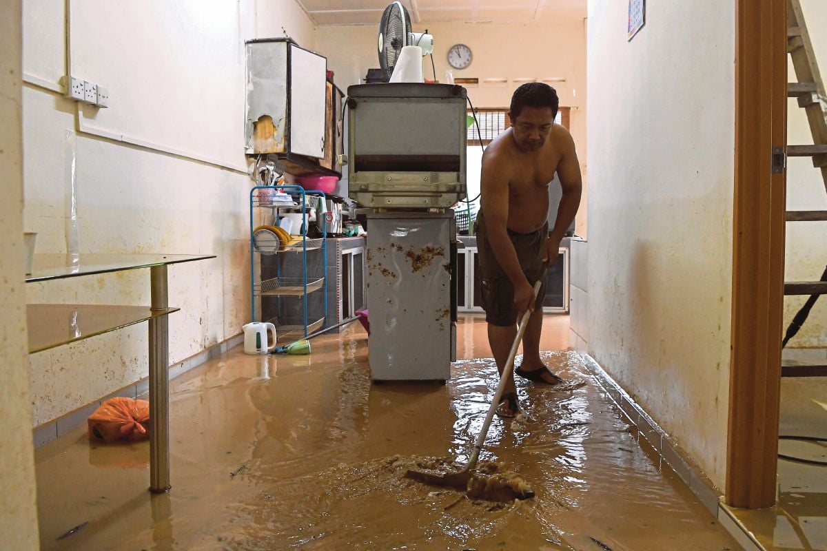 ZULKIFLI membersihkan kediamannya yang dinaiki air sehingga lebih satu meter akibat banjir kilat semalam ketika tinjauan hari ini. FOTO Bernama