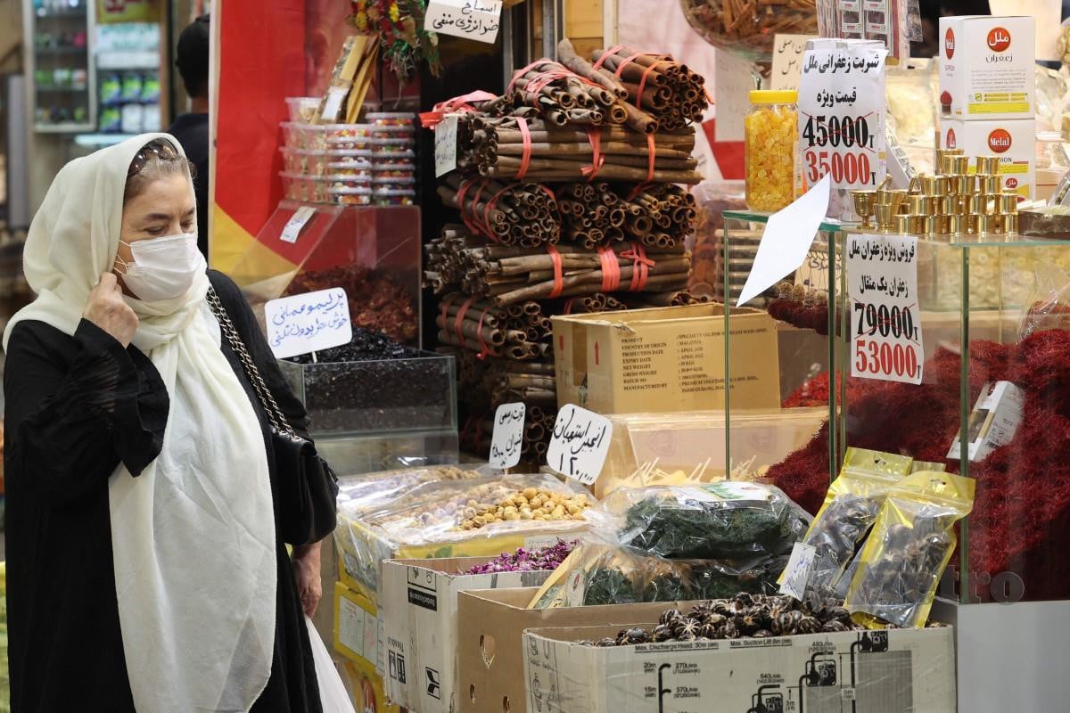 Seorang wanita memakai pelitup muka membeli barangan di Tajrish Bazaar di Tehran. - FOTO AFP