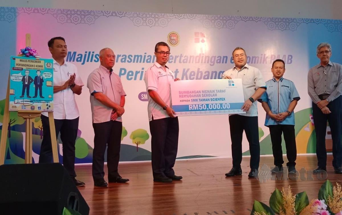 ABDUL Hadi Ali (tiga dari kanan) menyerahkan replika cek RM50,000 kepada Pengetua SMK Taman Scientex, Mohd Azmi Abdul Rahman (tiga dari kiri). FOTO Izz Laily Hussein