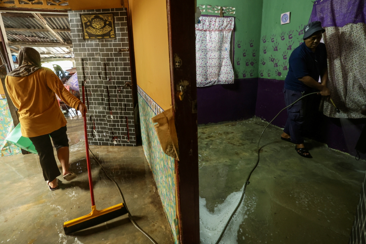 PENDUDUk  Kampung Tenang mencuci kediaman mereka selepas dinaiki air susulan banjir.FOTO Bernama