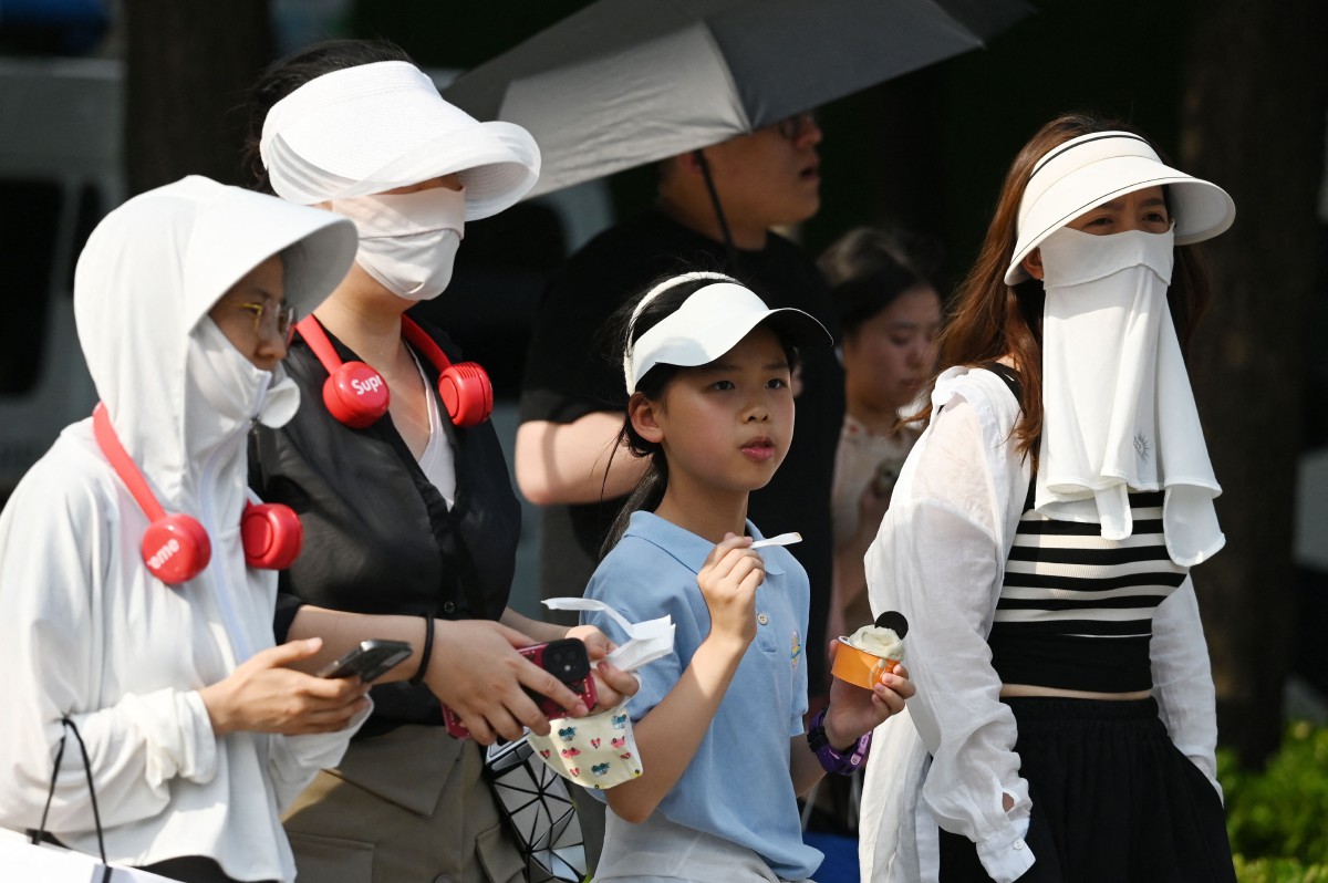 Orang ramai memakai pelindung kepala ketika cuaca panas di Beijing. - FOTO AFP