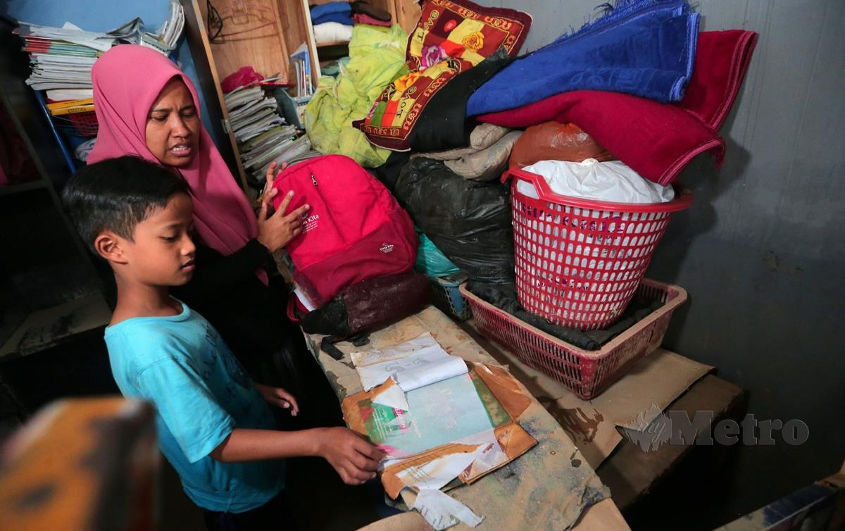 IBU bersama anaknya melihat buku dan baju sekolah yang musnah akibat banjir yang melanda rumahnya. FOTO Nur Aisyah Mazalan