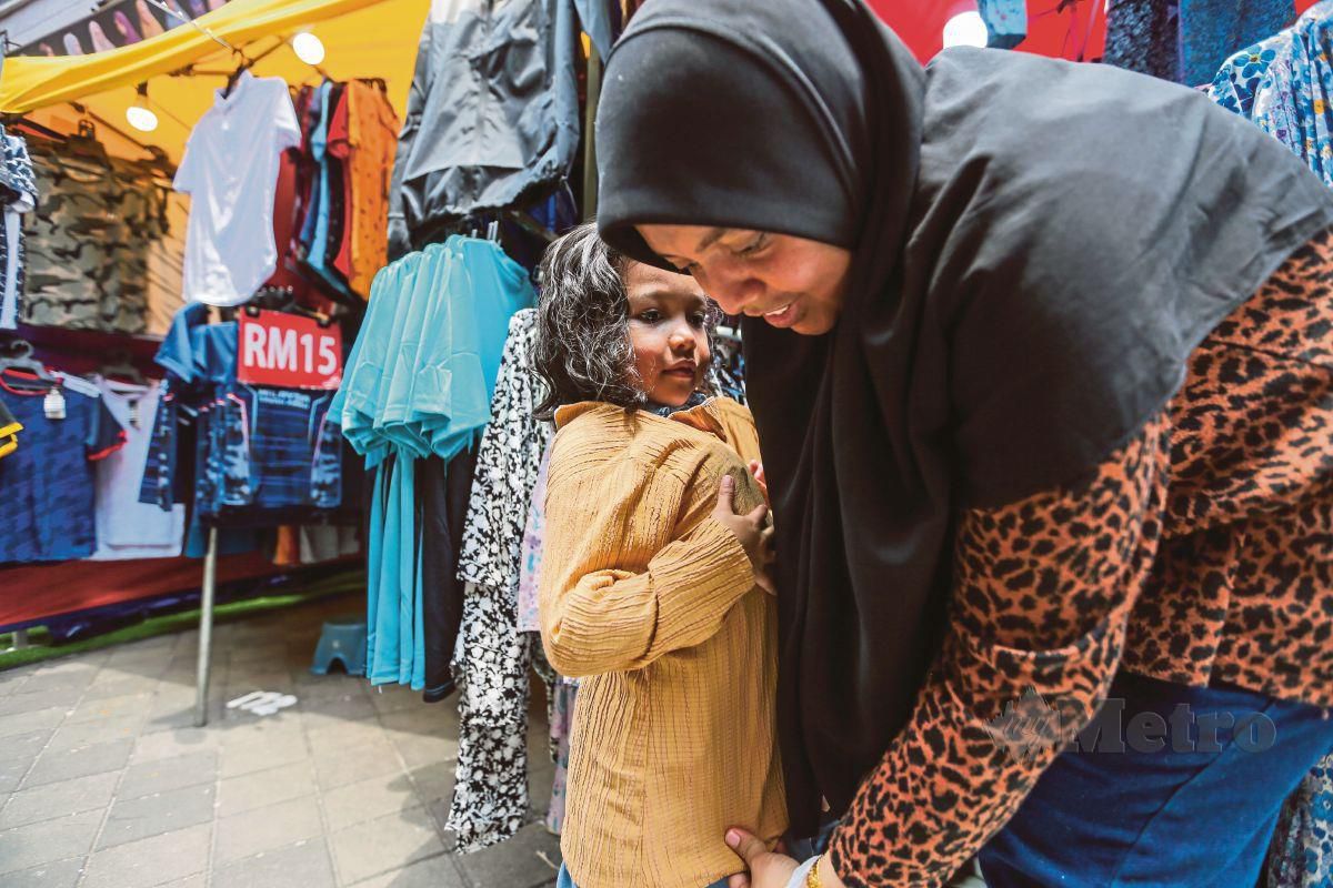 NORAIN (kanan) membeli baju raya anaknya pada tinjauan di Bazar Aidilfitri KL @ Lorong TAR. FOTO Aswadi Alias